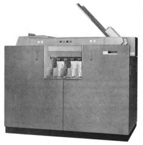 IBM Lochkartenleser und -stanzer
etea 150 cm hoher grauer Metallschrank mit Schräger Metallplatte von der rechten Seite nach links oben mit einem Stapel Lochkarten. In der Front oben einige Bedinertasten und unten in der Mitte 5 Ablagefächer für Karten