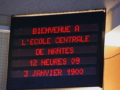 Schwarze Anzeigetafel in einer Französischen Schule mit roten Grossbuchstaben: "BIENVENUE A L'ECOLE CENTRALE DE NATES
12 HEURES 09
3. JANVIER 1900"
