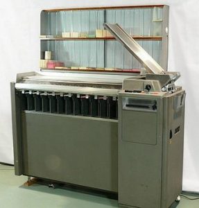 IBM Karten-Sortierer:
graue metallschrank mit den  Massen von ungefähr 120 cm hoch, 200 cm breit und 50 cm tief; rechts die schräge Karteneinzugsrampe; eine  Metallplatte ragt von der rechten Seite nach links schräg oben etwa 1 m lang; dort werden die Kartenstapel draufgelegt, von wo sie in den Sortierer reingeziogen werden können.
Auf der rechten Seite ist die etwa 50 x 50 cm grosse Steuereinheit mit den Bedienknöpfen. Auf der linken 150 cm breiten Seite des  grauen Monsters  sind 12 Fächer für die abgelegten Karten.
Auf der Oberfläche ist das Transportband