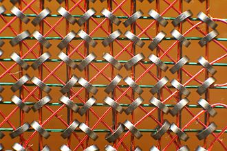 Magnetkernspeicher 
hellorange Plastikkarte mit schwarzen Drahtgitternetz 
und roten diagonal verwobenen Drähten; darin sind die kleinen runden silbergrauen Magnete angebracht.
